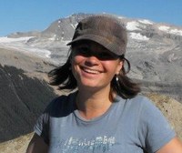 A woman wearing a hat stands against a mountain backdrop