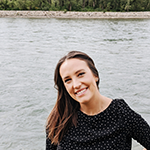 A woman with dark brown hair and a dark blouse standing by a river