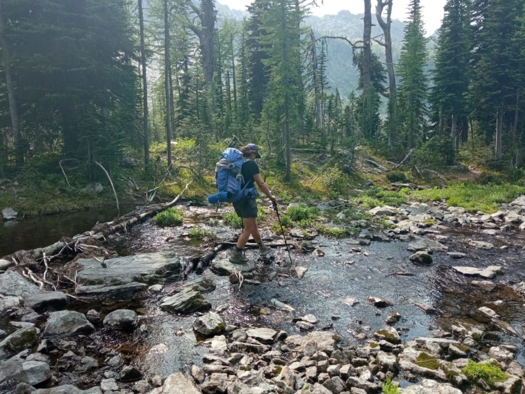 A person hiking crosses a small stream