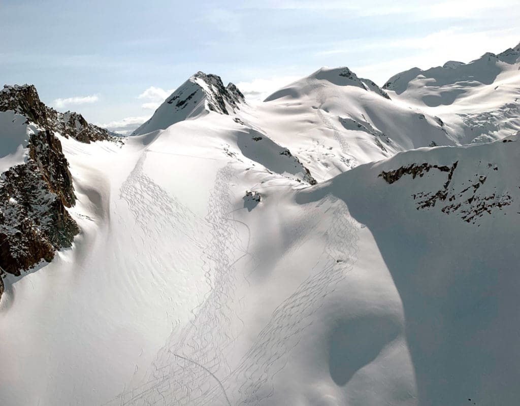 Dozens of ski touring tracks are seen in the snow going down the side of a large mountain.