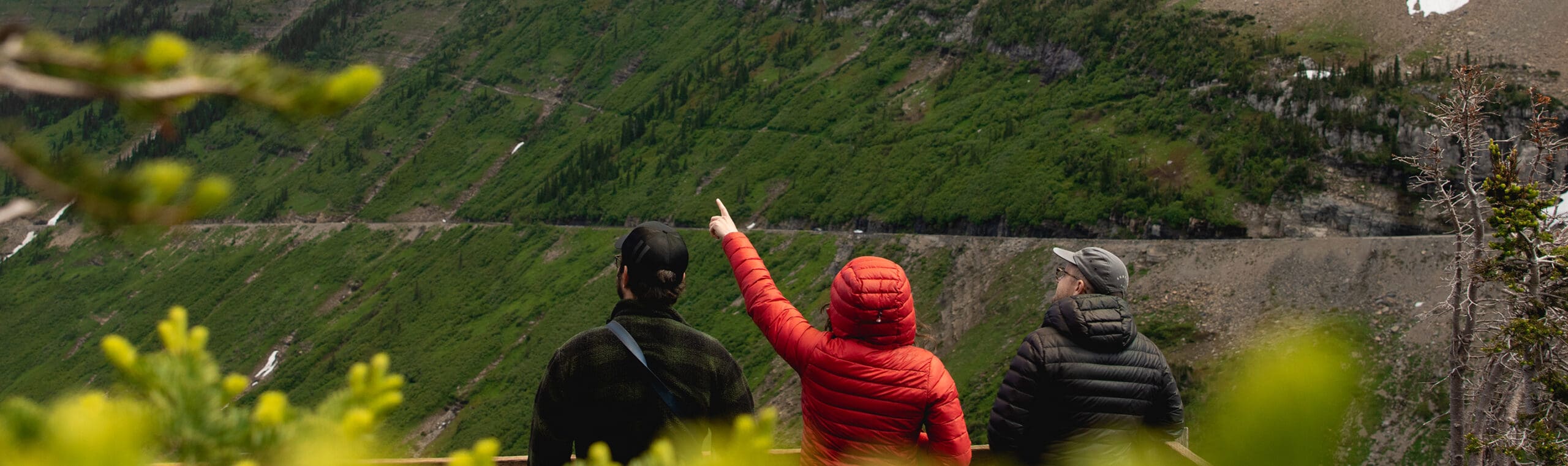Three people point to a cloudy mountain landscape in Glacier National Park
