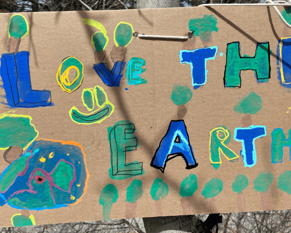 A cardboard sign painted by young students reading 'Love the Earth' in blue, yellow and green