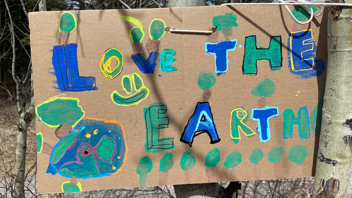 A cardboard sign painted by young students reading 'Love the Earth' in blue, yellow and green