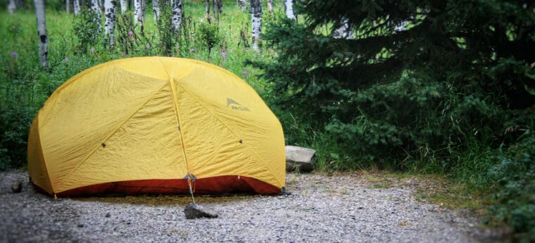 A yellow tent on a camping pad in the forest