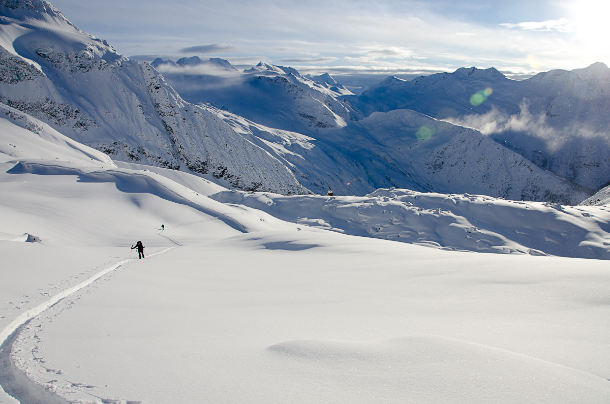 People hike up a snowy mountain scene with skis on their backs