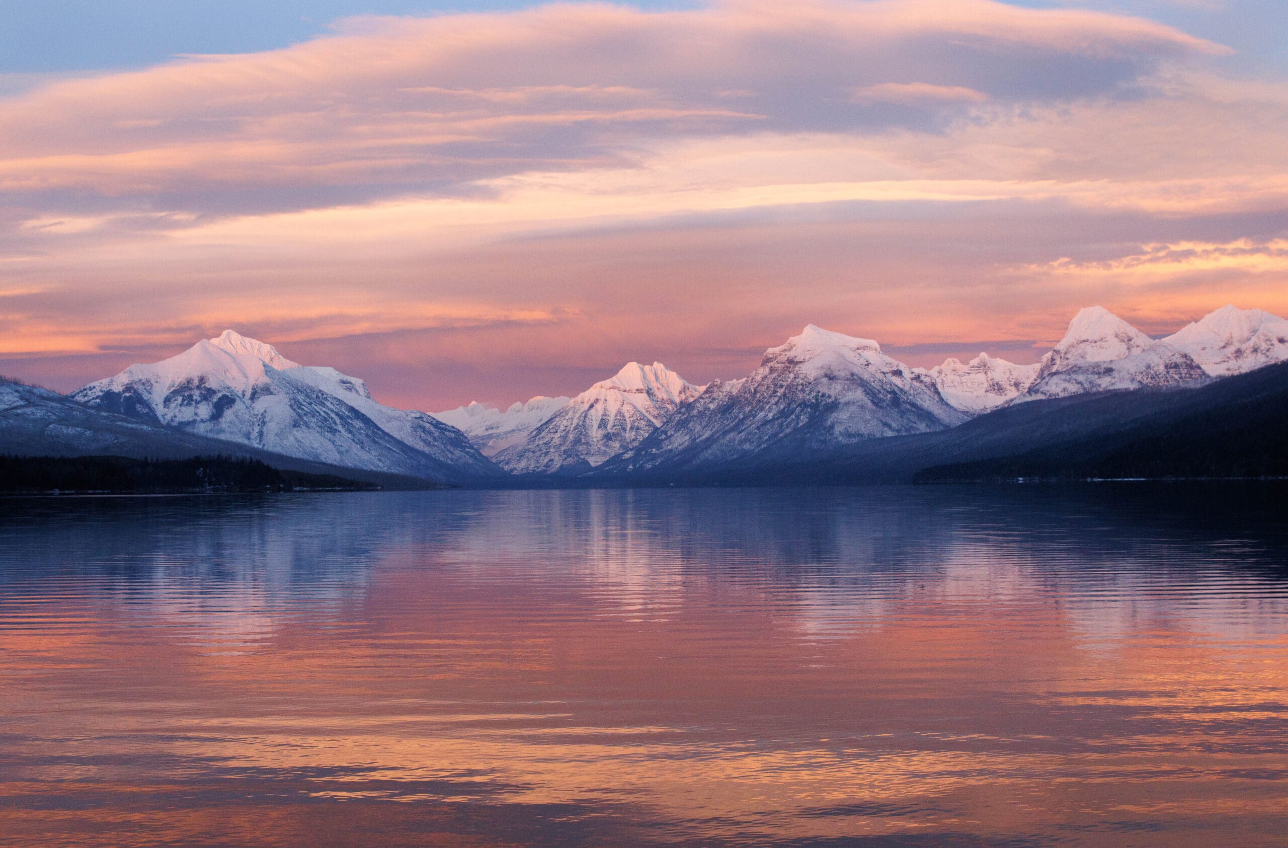 A mountain lake scene where the sky and mountains (and their reflection in a lake) appears pink with alpenglow