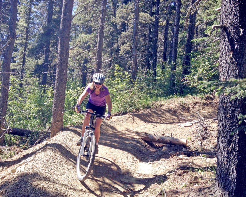 A person rides a mountain bike on a dirt trail through pine trees